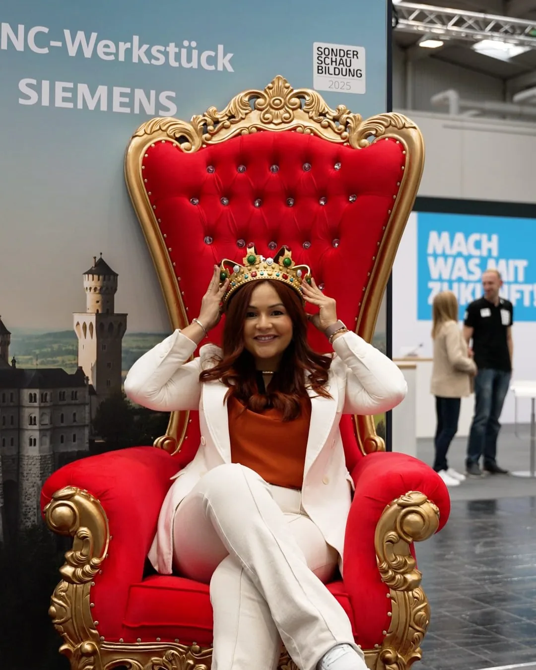 Vanessa Loiola de coroa em um trono vermelho e dourado em evento de tecnologia