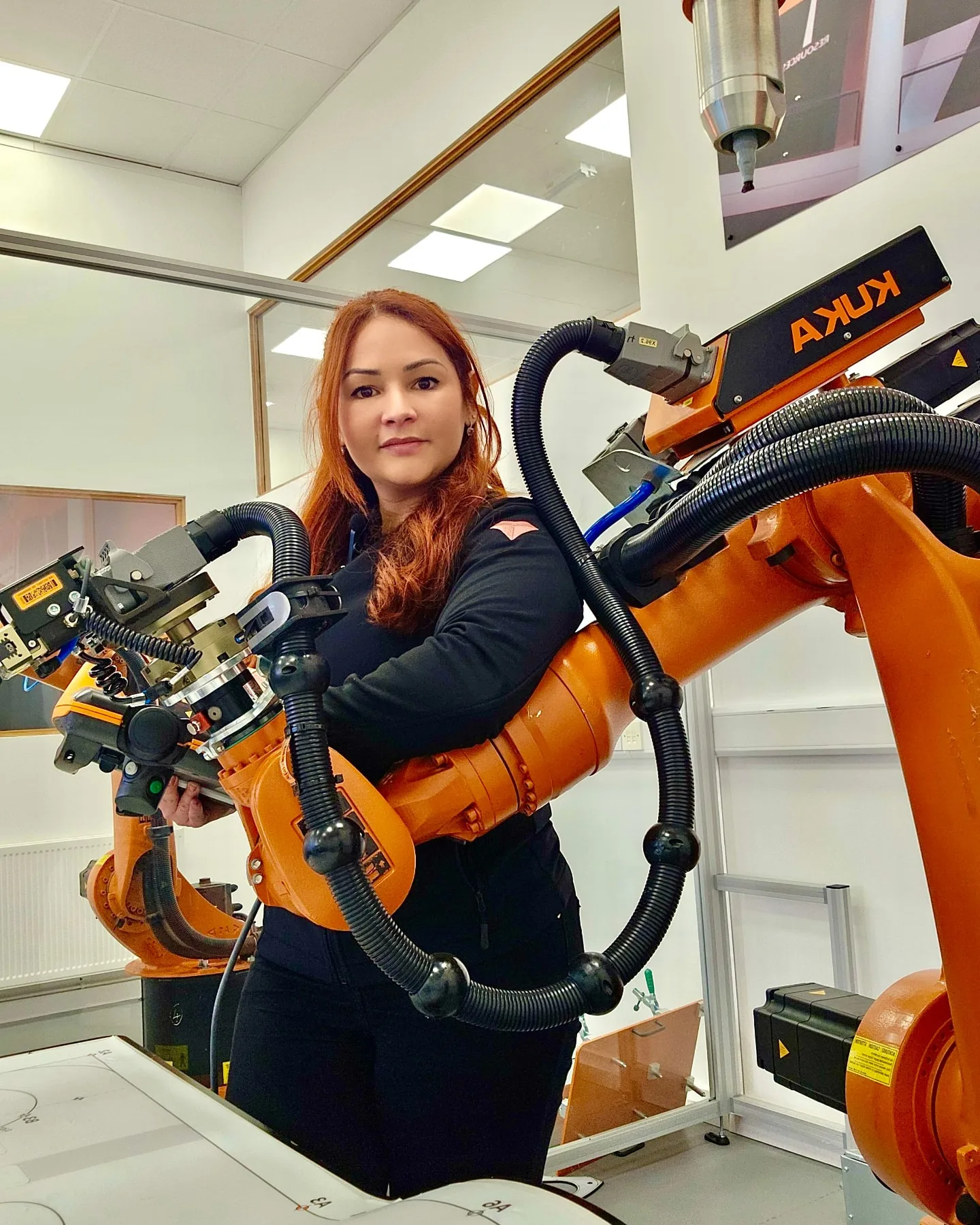 Vanessa Loiola ao lado de um braço robótico industrial KUKA laranja