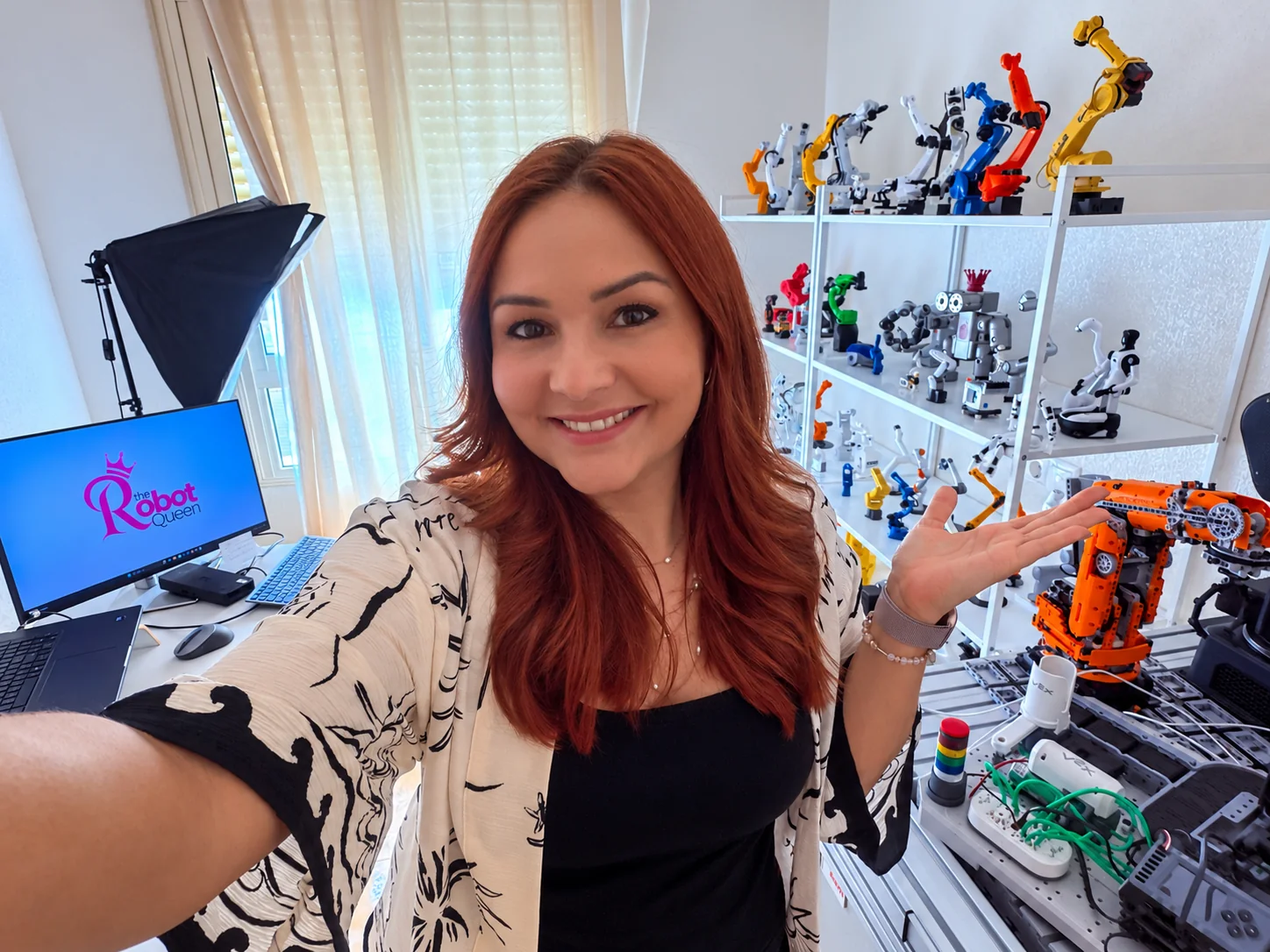 Vanessa Loiola in her robotics studio with robot arms and the Robot Queen logo