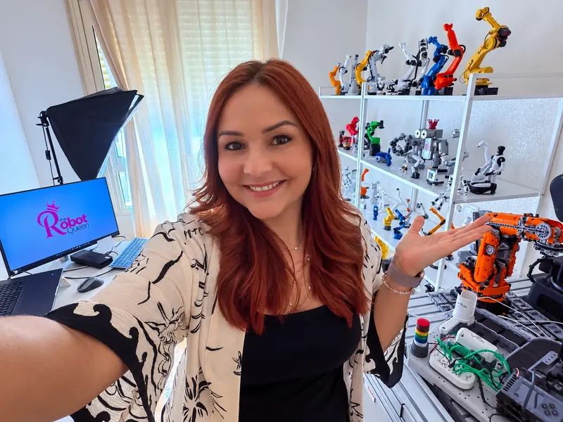 Vanessa Loiola in her robotics studio with robot arms and the Robot Queen logo
